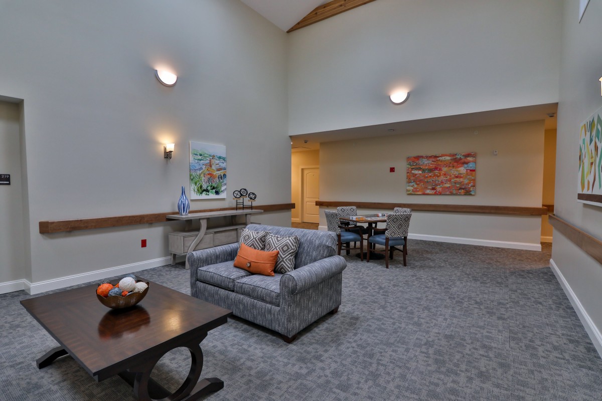 A cozy living room with a sofa, table, and decorative wall art, featuring warm lighting and a carpeted floor.