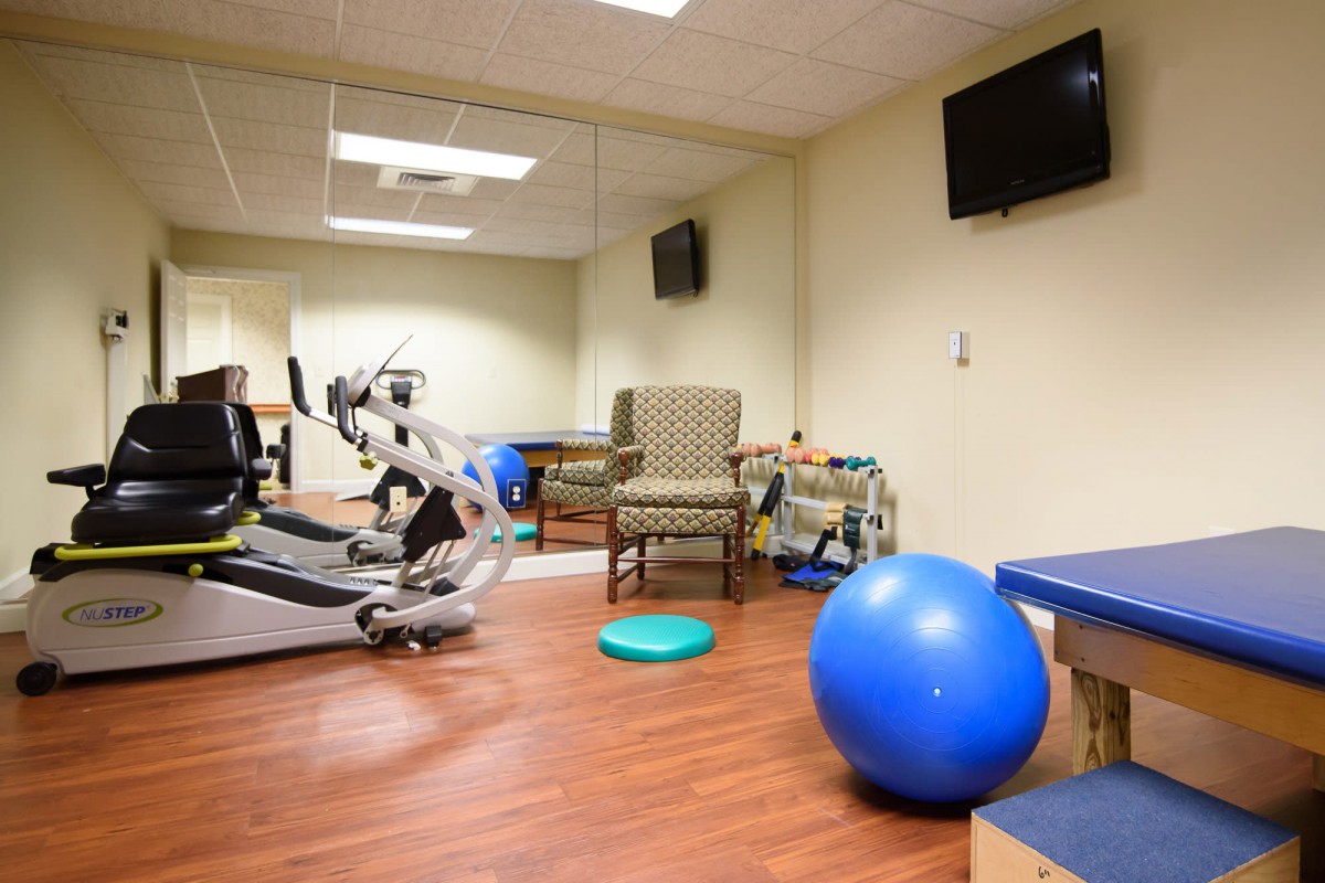 A small gym room equipped with exercise machines and a blue exercise ball.