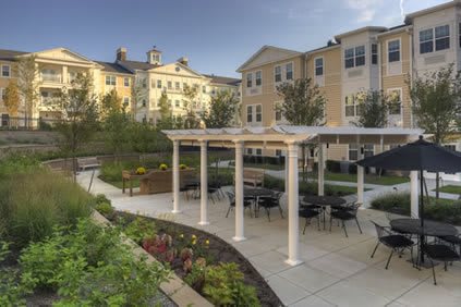 A beautifully landscaped outdoor seating area with a pergola in front of an apartment building.
