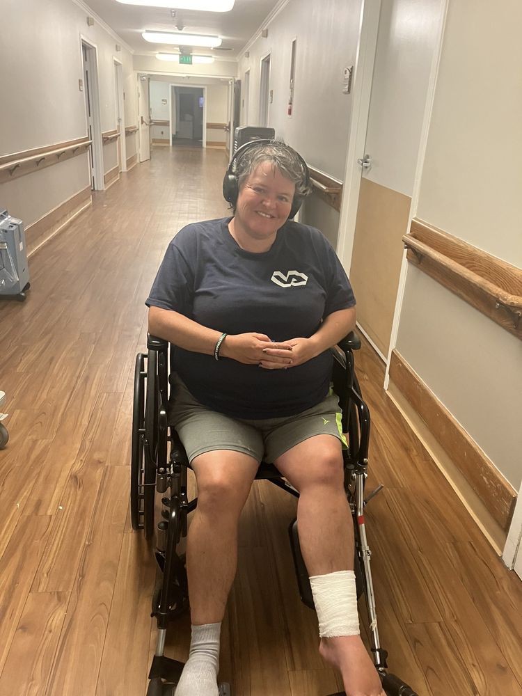 A person sitting in a wheelchair wearing headphones and smiling in a hallway.