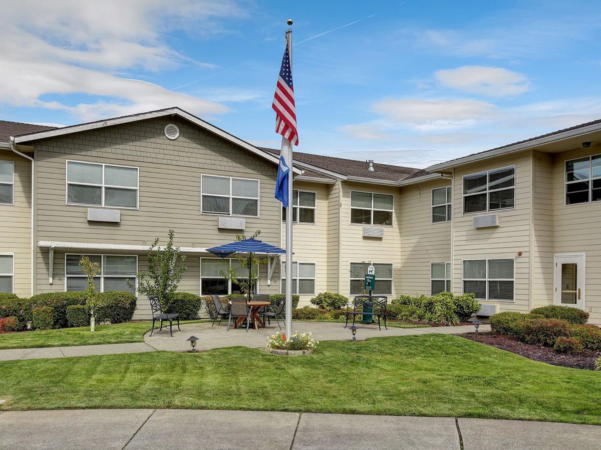 A two-story building with an American flag in front, surrounded by a well-manicured lawn and outdoor seating area.