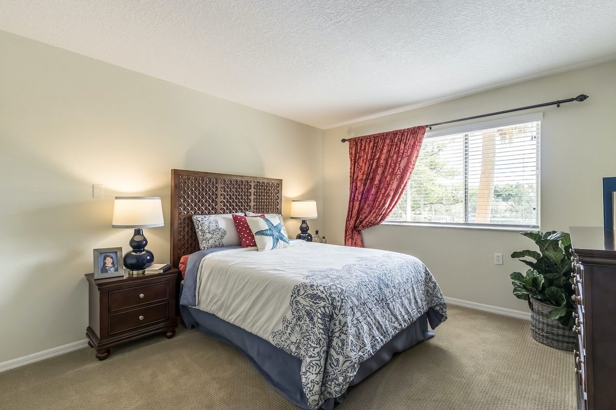 A cozy bedroom with stylish decor, featuring a bed, bedside tables with lamps, and a window with red curtains.