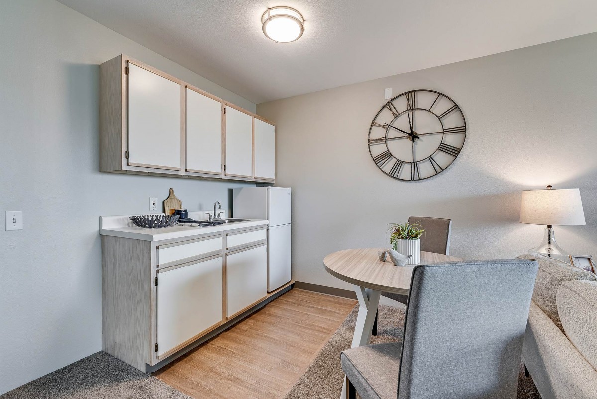 A modern minimalist kitchen with white cabinetry and a round dining table, accented by a large wall clock.