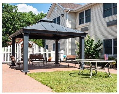 A cozy outdoor patio area with a gazebo, benches, and a table set in the garden beside a house.