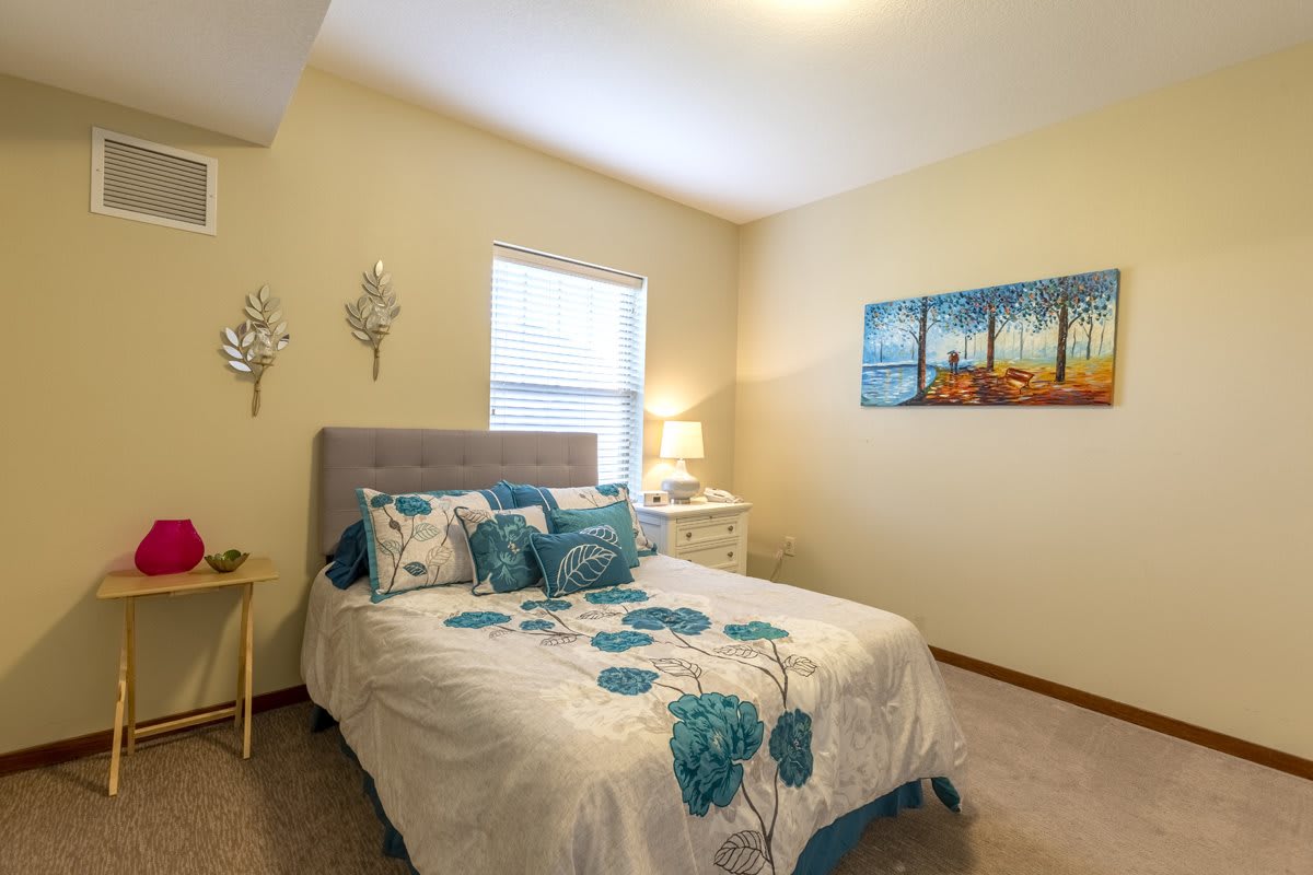 A cozy bedroom with a neatly made bed, floral bedding, and decorative artwork on the wall.