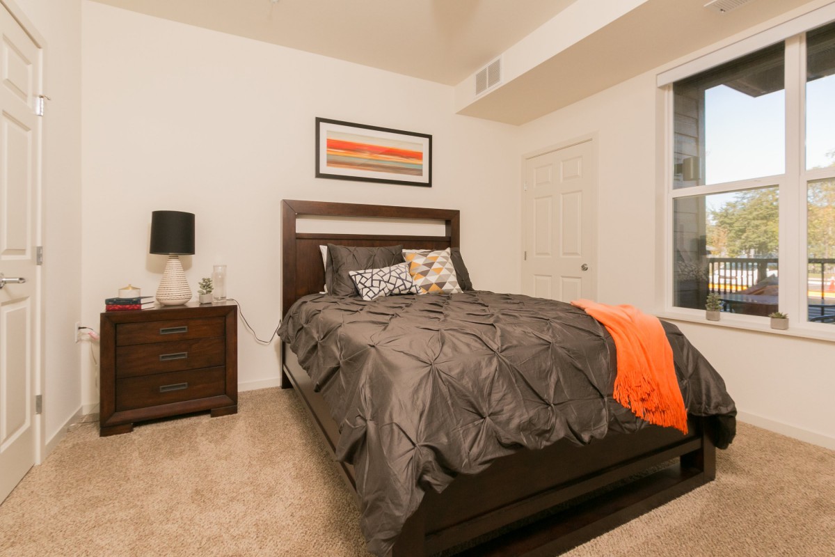 A modern bedroom with a neatly made bed, featuring dark furniture and colorful accents.