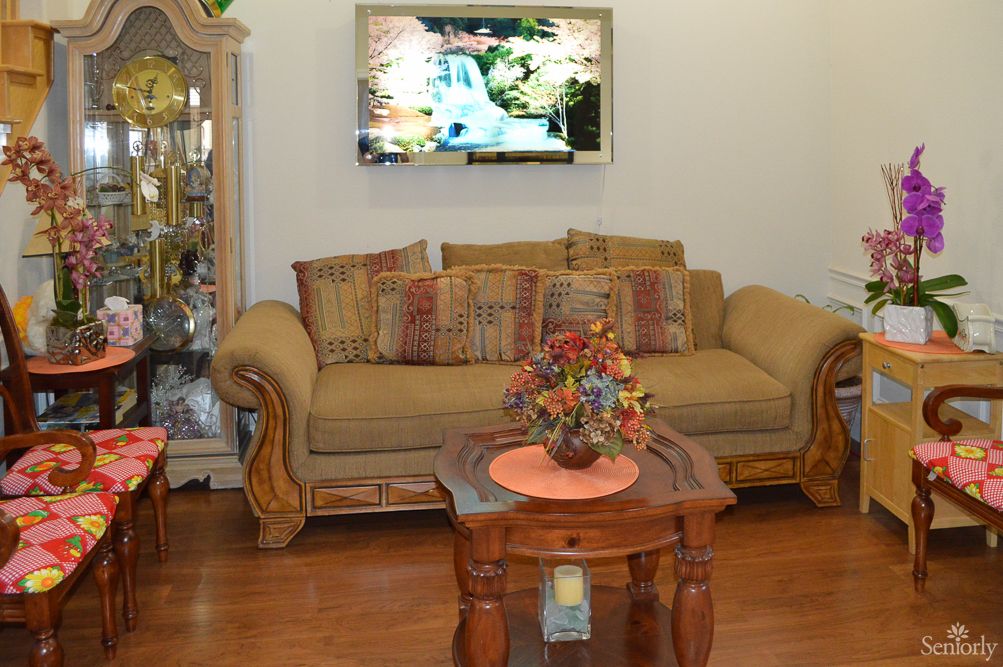 A cozy living room with a sofa, coffee table with a flower arrangement, and a TV mounted on the wall.
