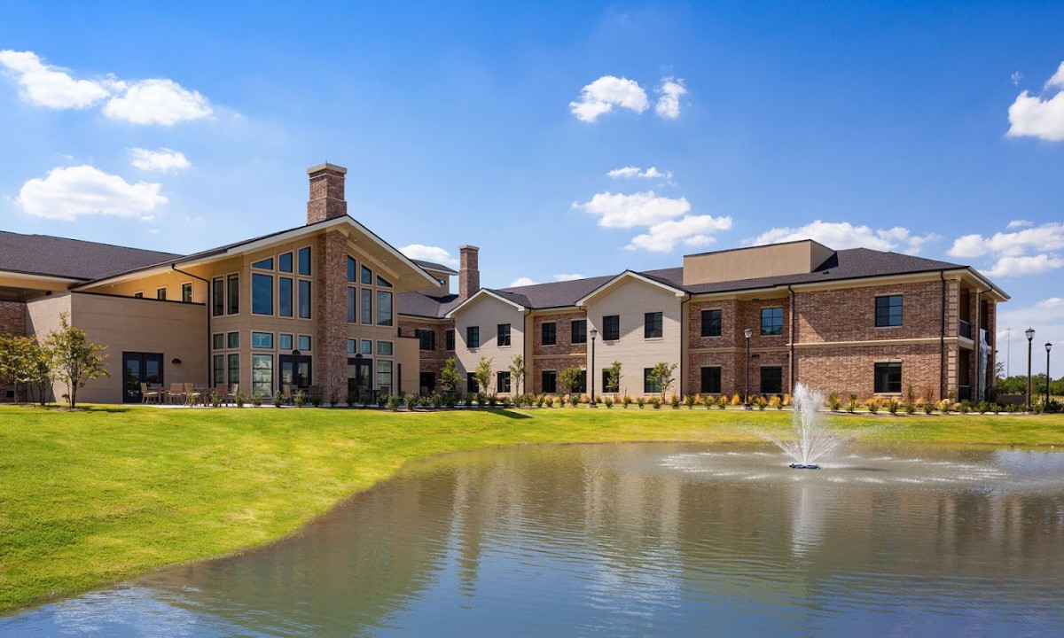 A scenic view of a large building with a pond and fountain in the foreground under a partly cloudy sky.