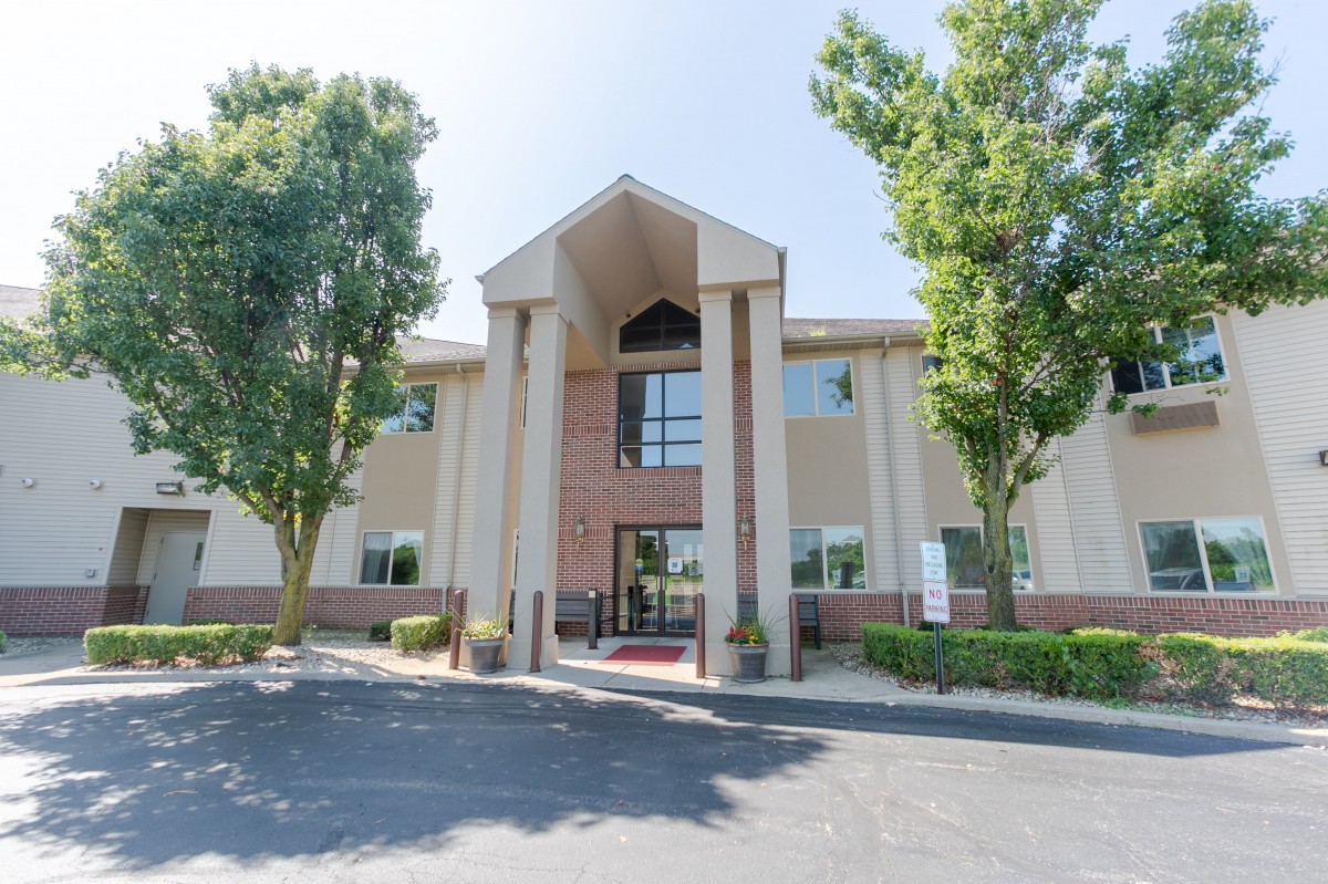 A modern office building with an entrance flanked by tall trees and a parking lot in front.