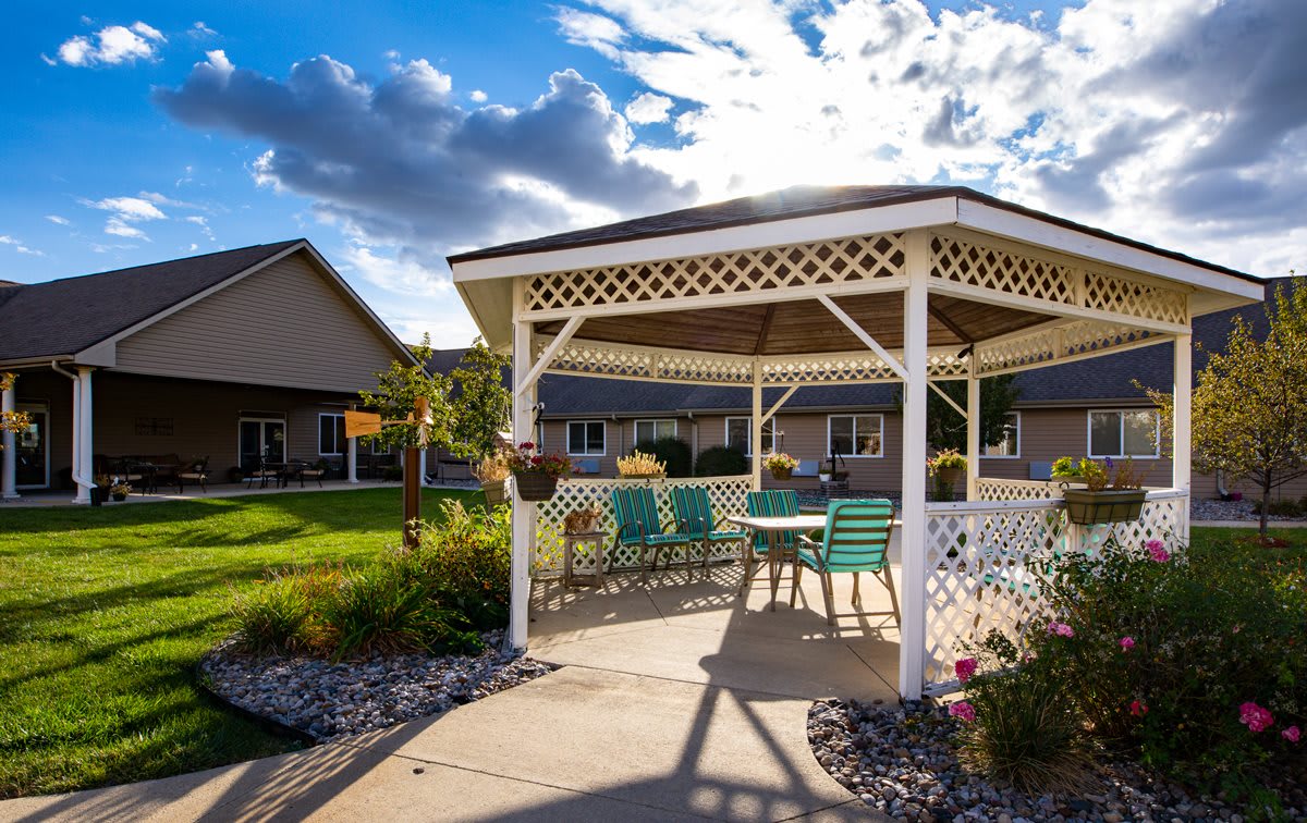 A sunny day in a residential garden featuring a white gazebo with patio furniture.