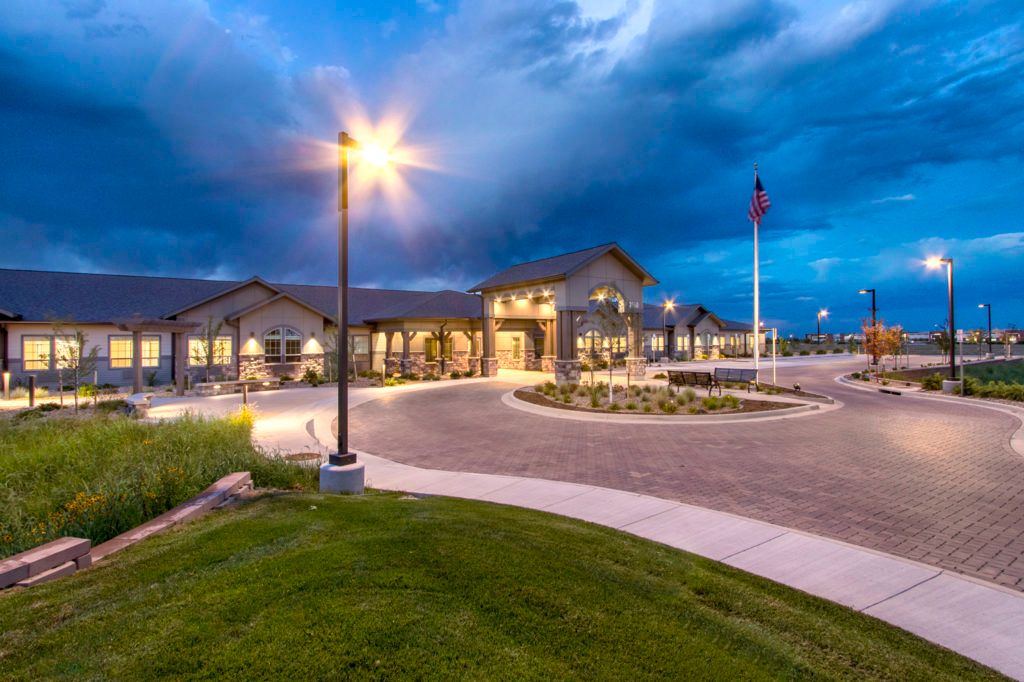 A well-lit building at dusk with a cloudy sky and landscaped surroundings.