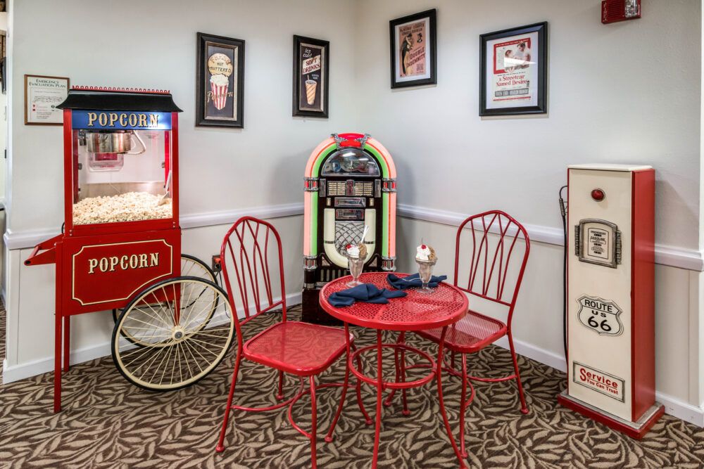 A retro-themed room featuring a jukebox, vintage-style red table and chairs, and a popcorn machine.