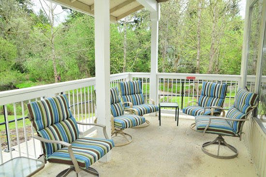 A cozy outdoor patio area with striped cushioned chairs and a small table, surrounded by greenery.