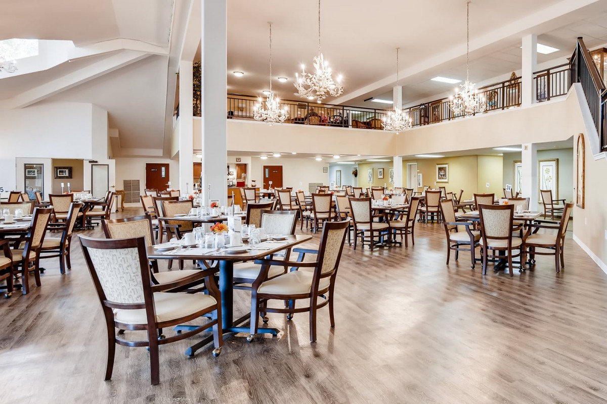 A spacious dining area with neatly arranged tables and chairs, illuminated by elegant chandeliers.