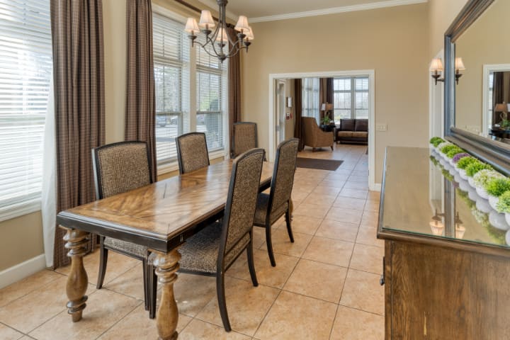 A dining room with a wooden table and chairs, featuring large windows and a chandelier.