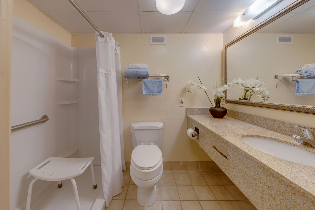 A clean and well-organized bathroom featuring a shower, toilet, sink, and mirror, with towels neatly arranged on a rack.