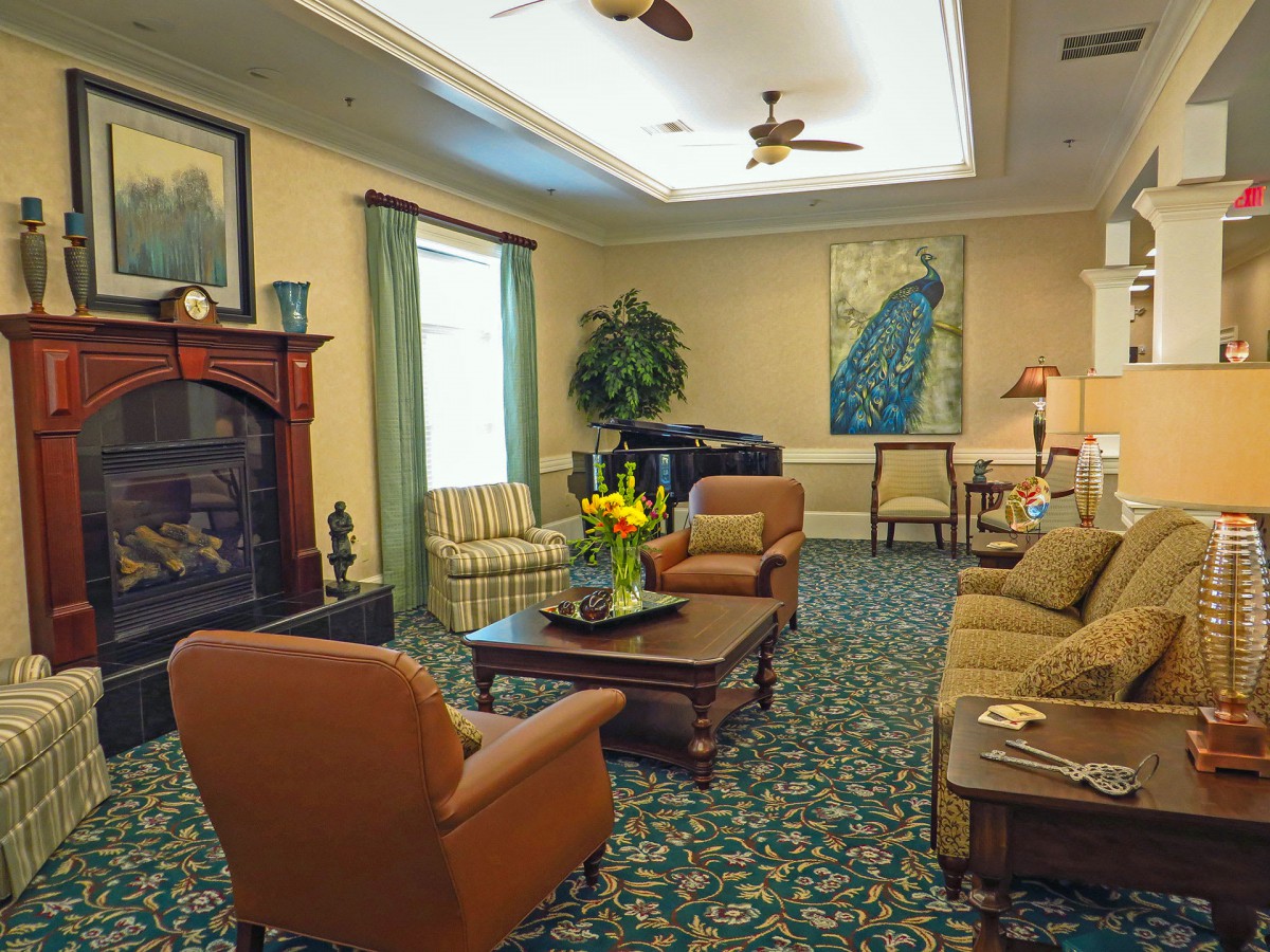 A cozy living room with sofas and chairs arranged around a coffee table, featuring a fireplace and decorative elements including plants and artwork.