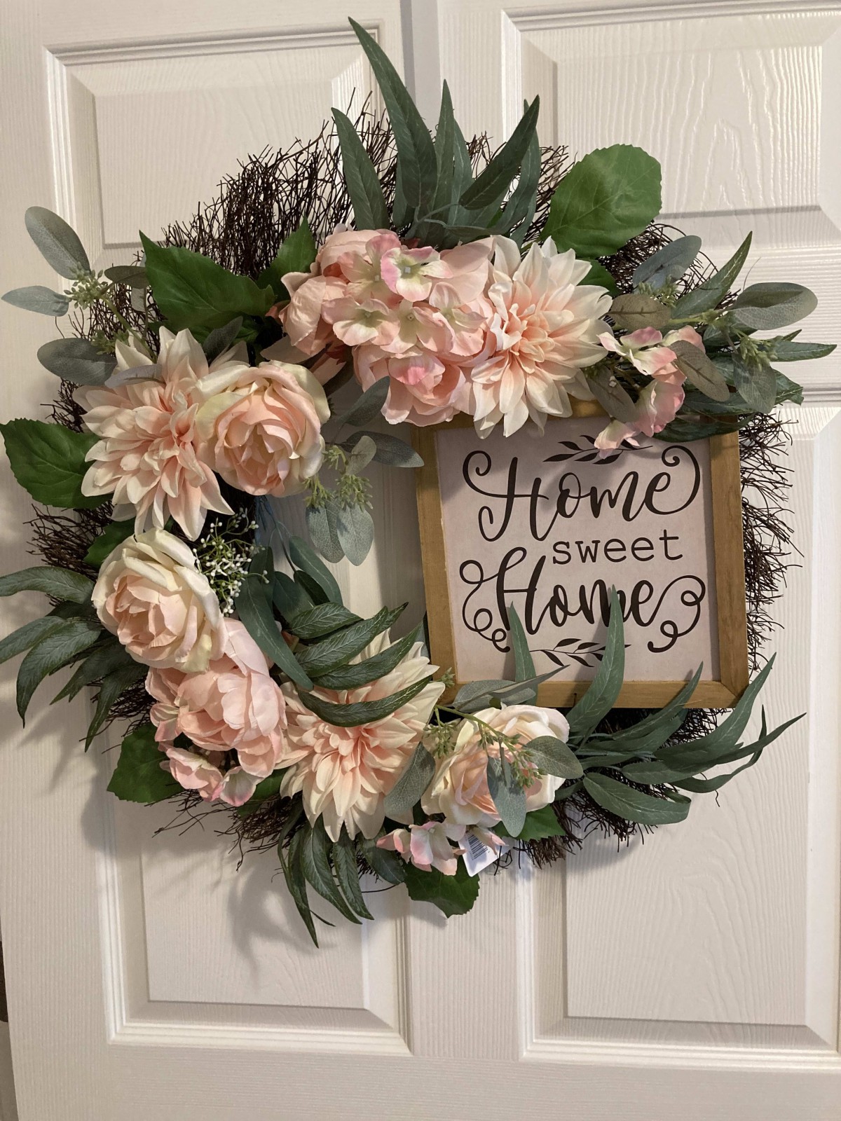 A decorative wreath with pink flowers and greenery surrounding a 'Home Sweet Home' sign.