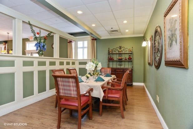 A cozy dining room with a neatly set table surrounded by chairs, featuring elegant decor and ambient lighting.