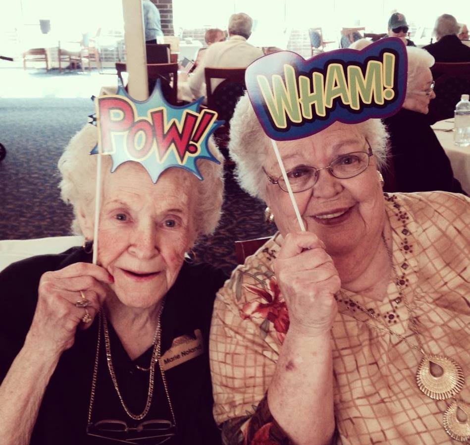 Two elderly women having fun with comic-themed props at a party.