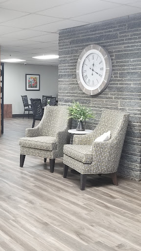 A cozy waiting area featuring two patterned chairs, a small table with a decorative plant, and a large wall clock.
