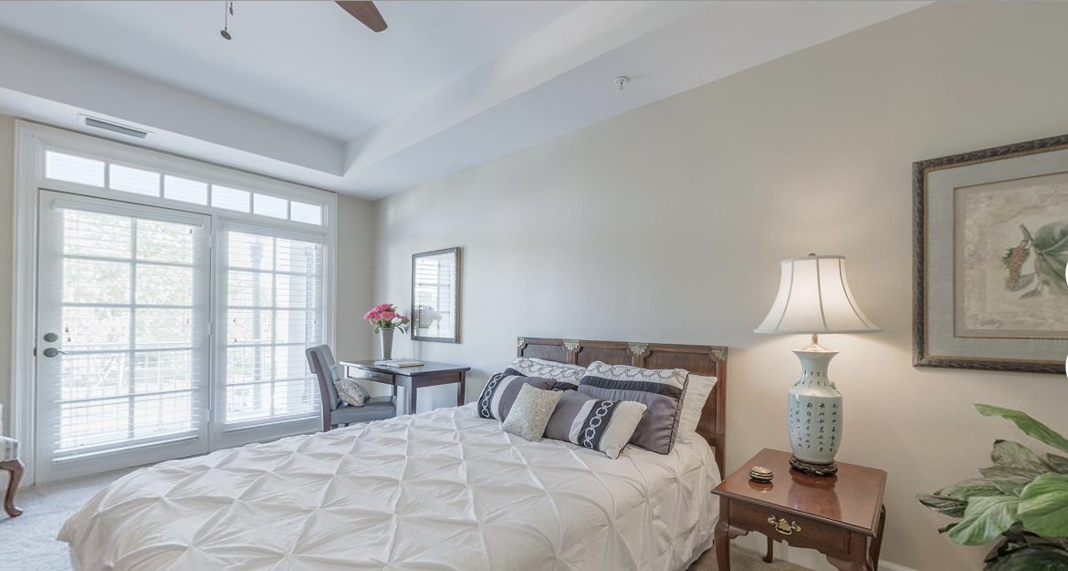 A cozy bedroom with a neatly made bed, side table, and a lamp, featuring soft lighting and elegant decor.
