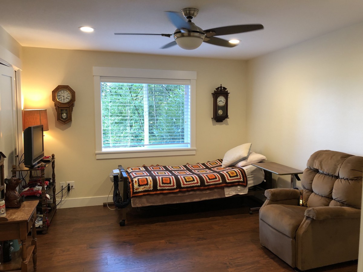 A cozy bedroom with a single bed, recliner, wall clocks, and a ceiling fan.