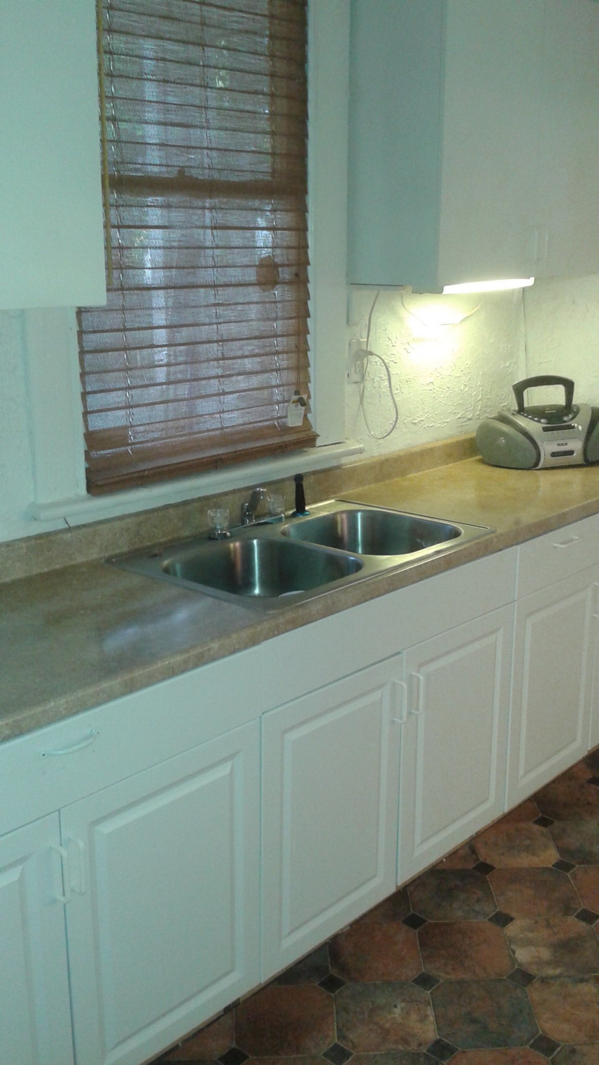 A kitchen with a double sink, countertop, and cabinets beneath a window with blinds.