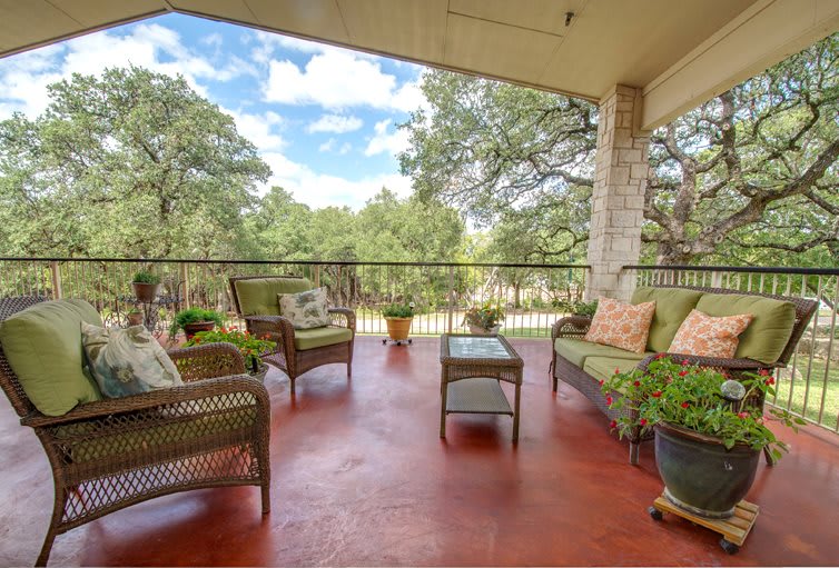 A cozy outdoor patio with wicker furniture and potted plants overlooking a scenic tree-filled landscape.