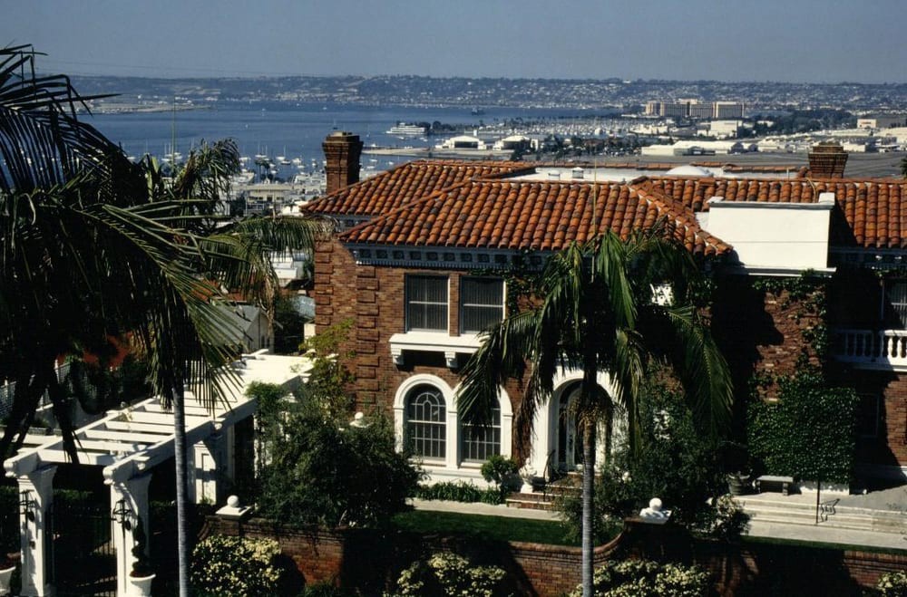 A Mediterranean-style house with a view of the water and lush palm trees.