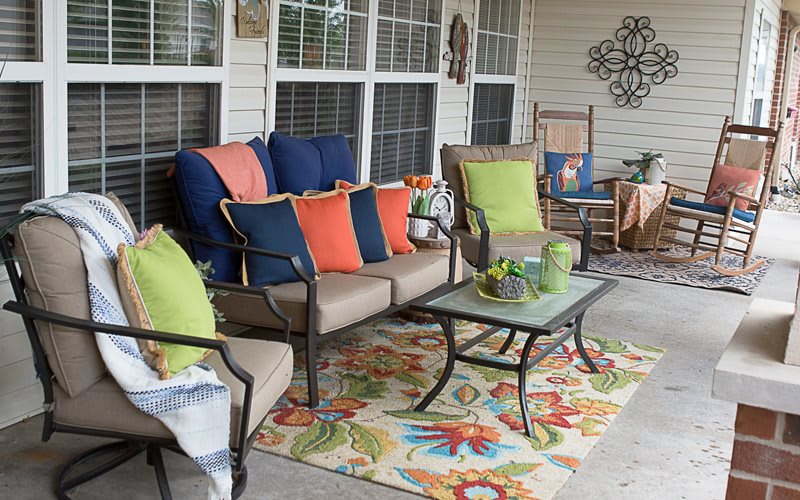 A cozy outdoor patio with colorful pillows, a patterned rug, and various furniture pieces.