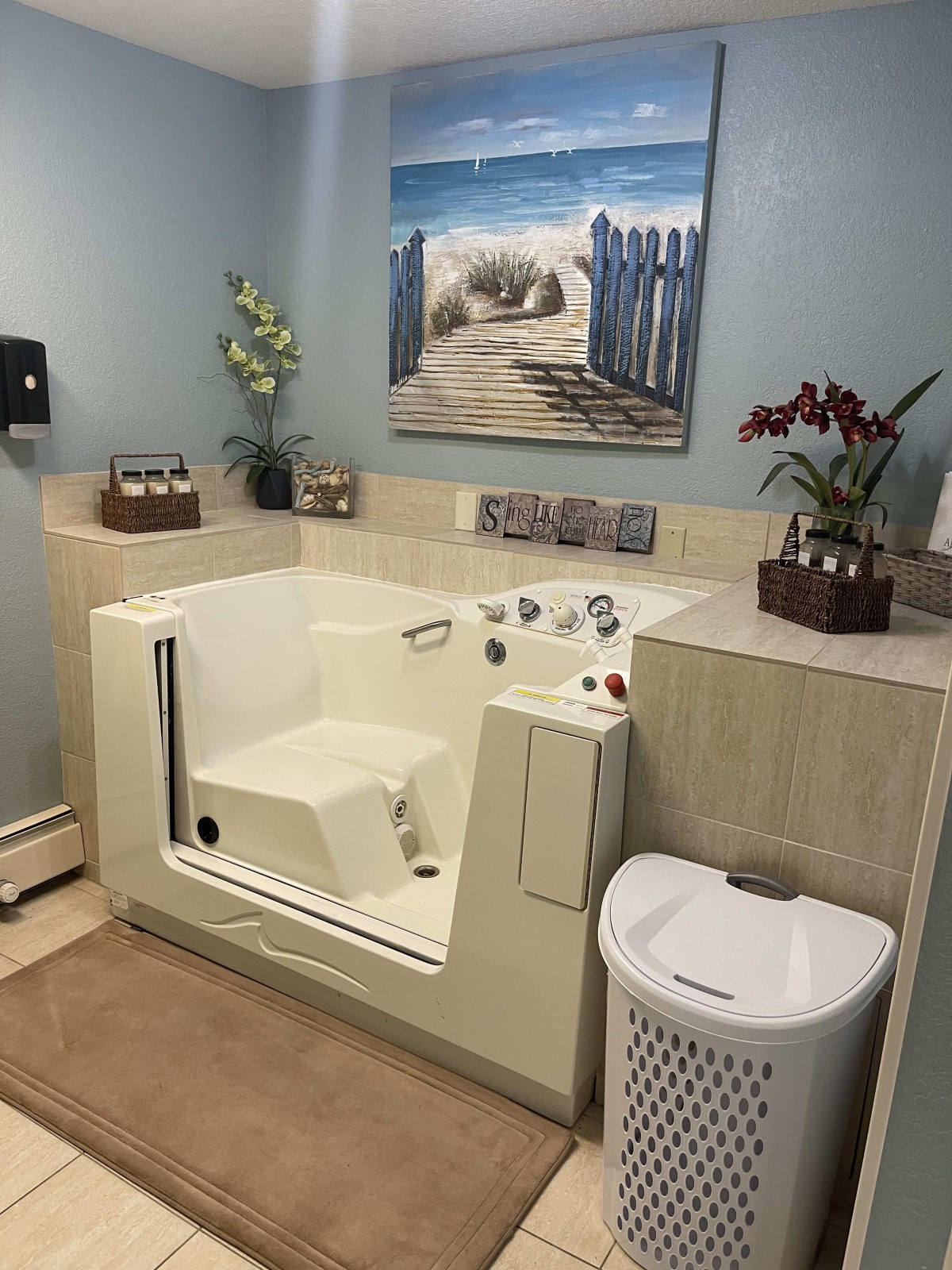 A bathroom featuring a walk-in tub, decorative plants, and beach-themed wall art.