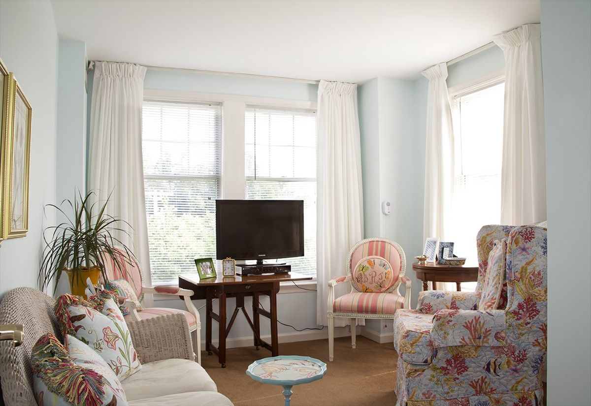 A cozy living room with floral furniture and large windows allowing natural light.