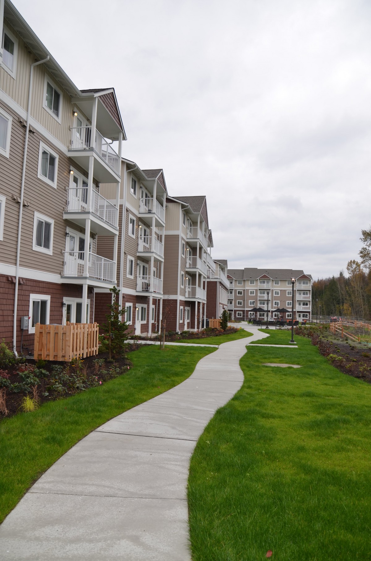 A row of modern apartment buildings with a winding sidewalk bordered by green grass.