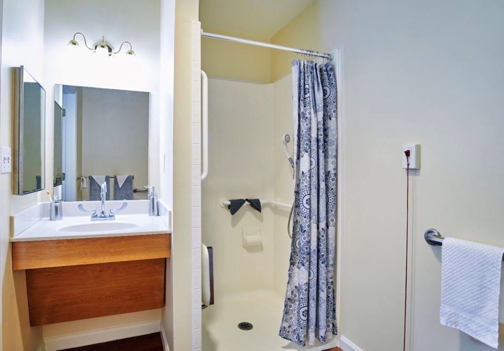 A small bathroom featuring a shower with a blue and white patterned curtain, a sink, and a mirror.