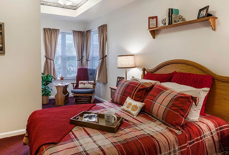 A cozy bedroom with red plaid bedding, a window with curtains, and a chair in the corner.
