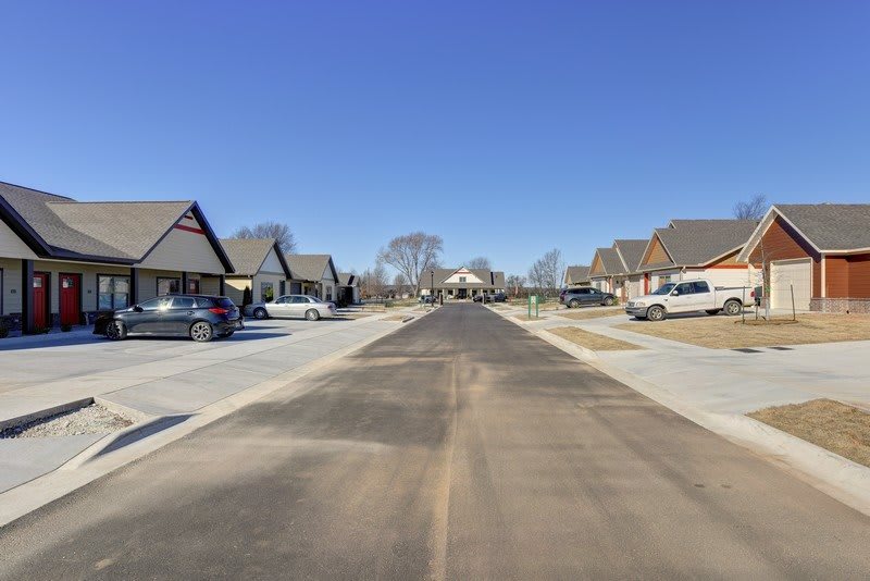 A quiet suburban street lined with houses and parked cars under a clear blue sky.