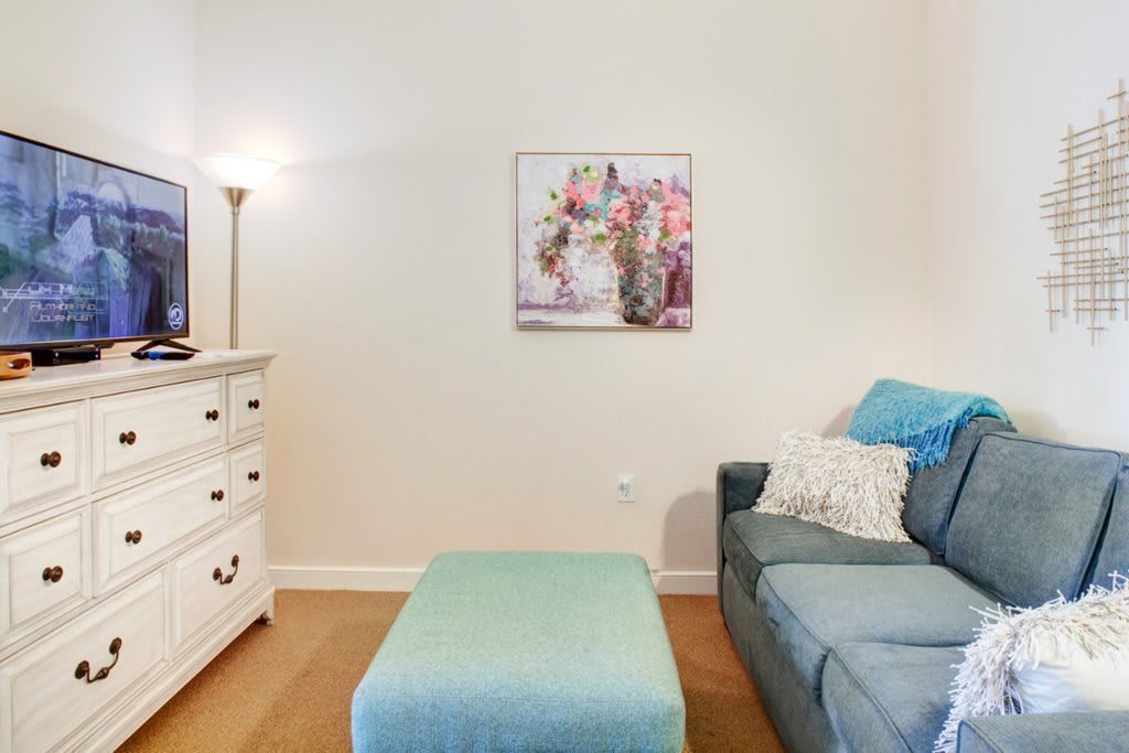 A cozy living room corner with a sofa, ottoman, dresser, and wall art.