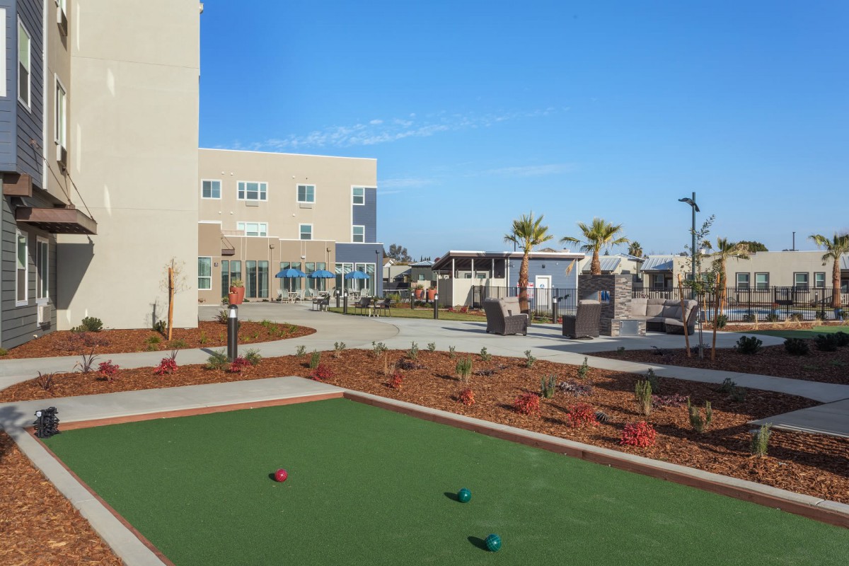 A sunny recreational area featuring a bocce court and landscaping near a modern building.