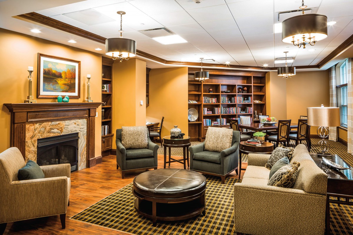 A cozy living room featuring a seating area with armchairs, bookshelves, and a fireplace.