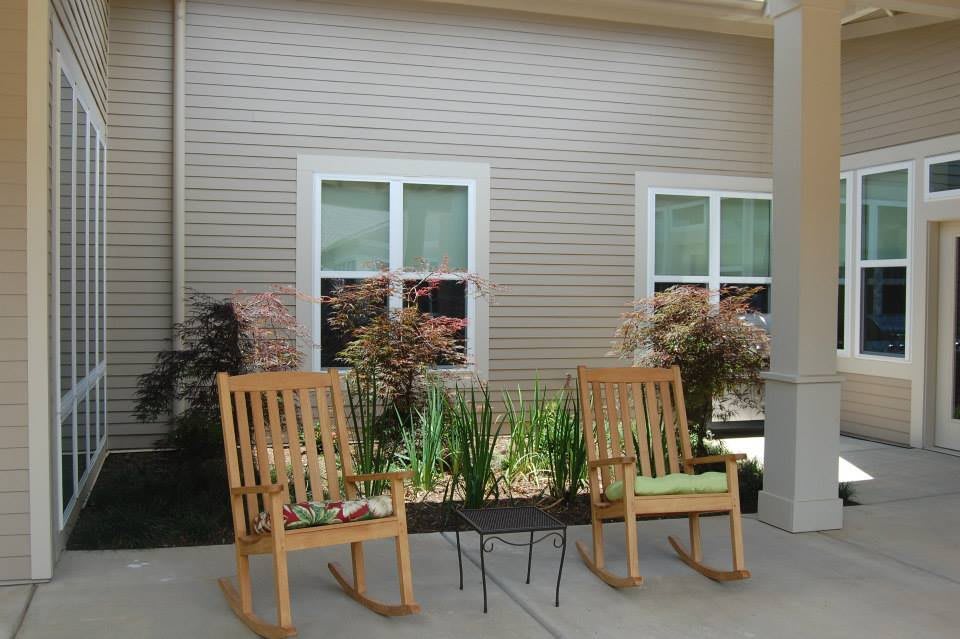 A cozy patio setup with wooden rocking chairs and plants against a building exterior.