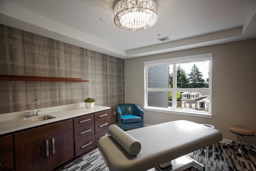 A modern spa room featuring a massage table, elegant chandelier, and ample natural light.