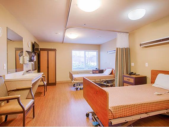 A clean and well-lit hospital room featuring two patient beds and a large window.