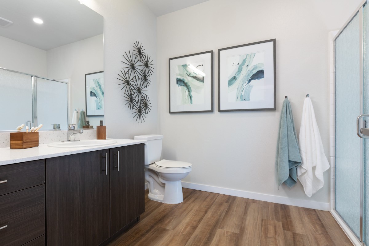 A modern bathroom with wood flooring, featuring artwork and a sleek vanity.