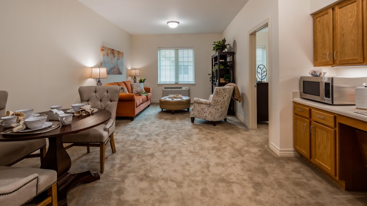 A cozy living room featuring a sofa and armchairs, with a dining table in the foreground and decorative elements throughout.