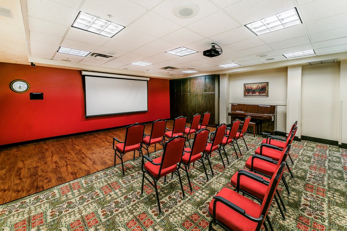 A well-lit conference room set up with rows of chairs facing a projector screen.