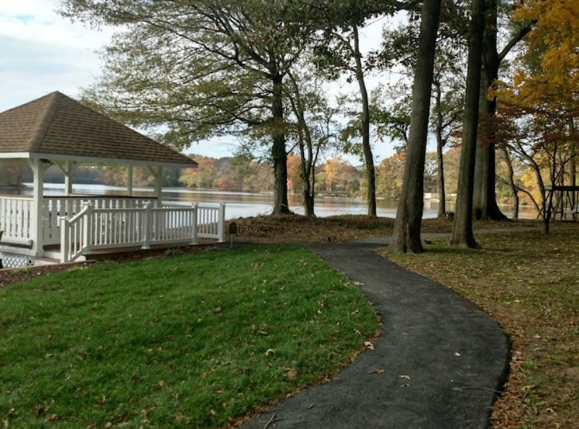 A peaceful park scene with a lake, trees, and a winding path leading to a gazebo.