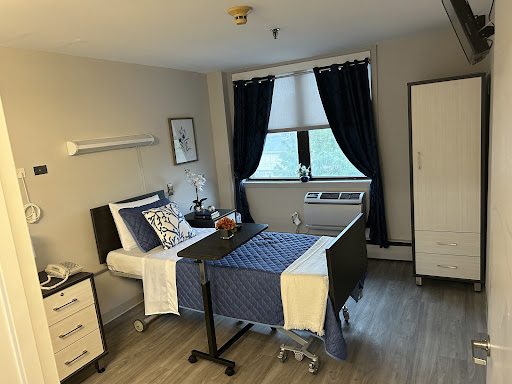 A tidy hospital room equipped for patient care, featuring a bed, wardrobe, and large window.