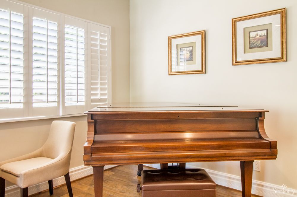 A room featuring a grand piano with framed art on the wall and a cozy chair by the window.