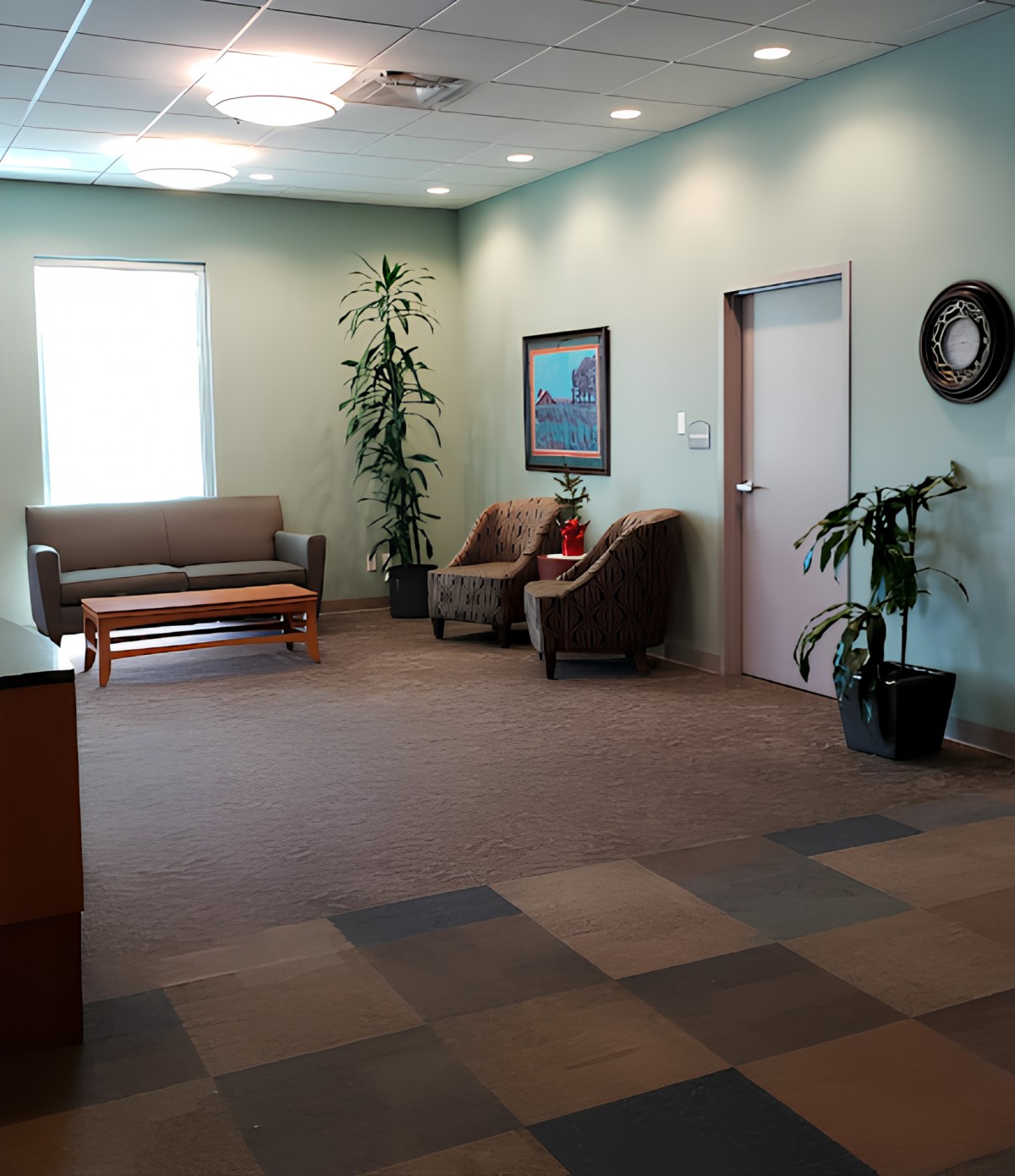 A spacious and well-lit waiting room with chairs, a sofa, and decorative plants.